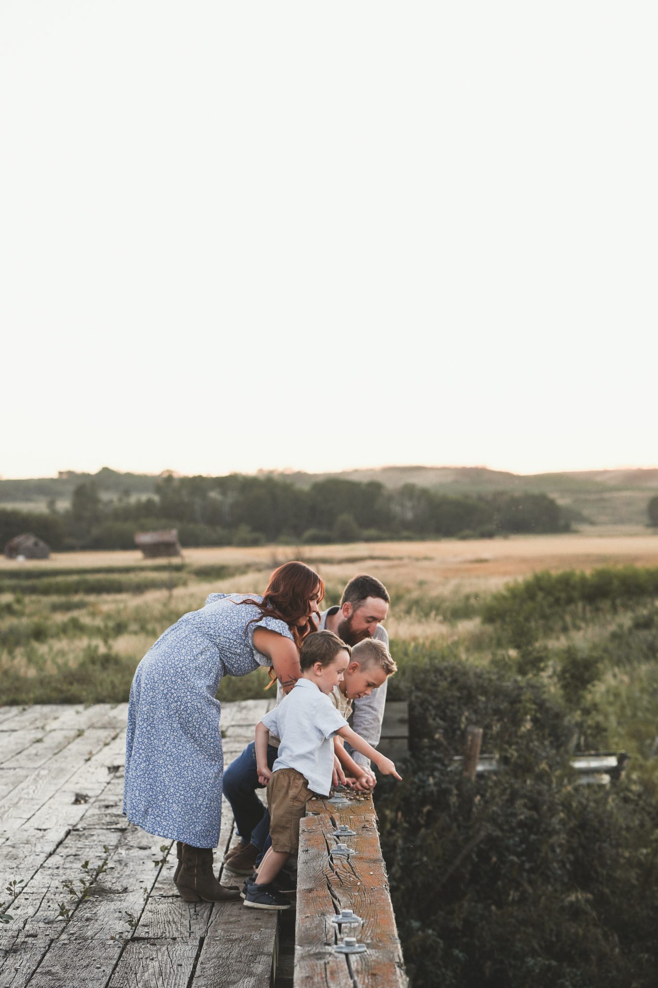 Rachael, her partner and their two boys peering over a wooden bridge railing