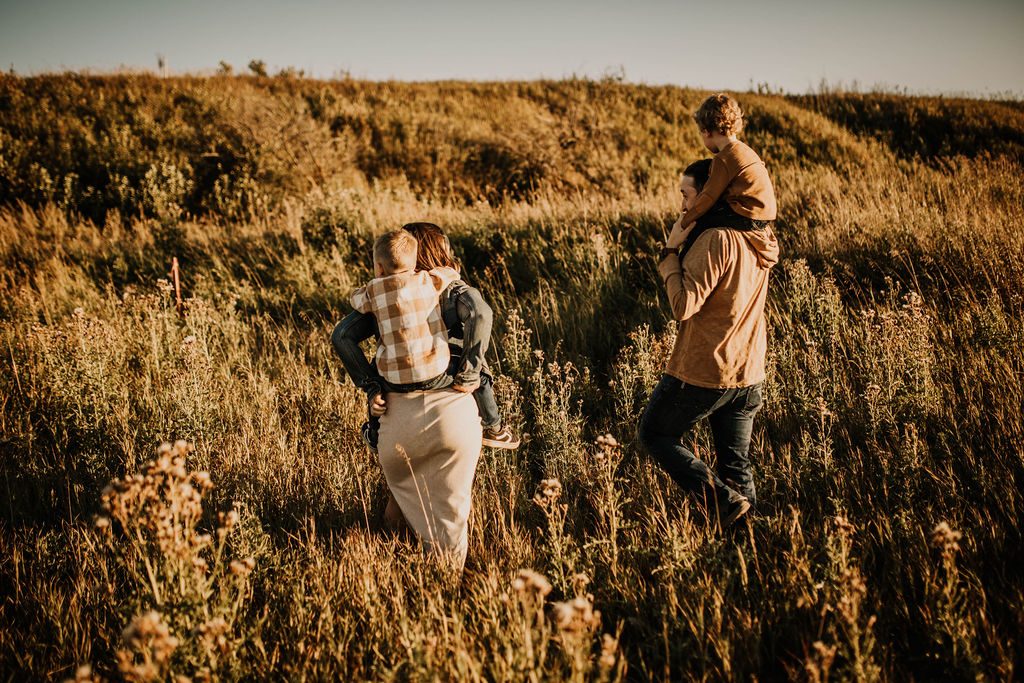 Rachael and her partner carrying their boys through tall prairie grass
