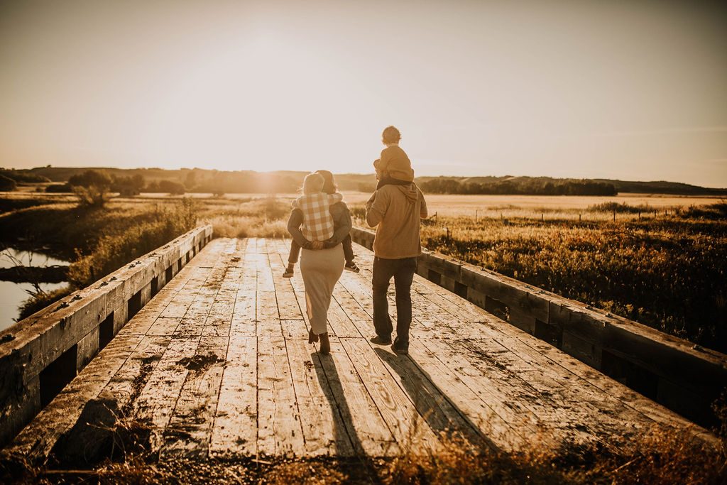 The family walking across an old wooden bridge at sunset